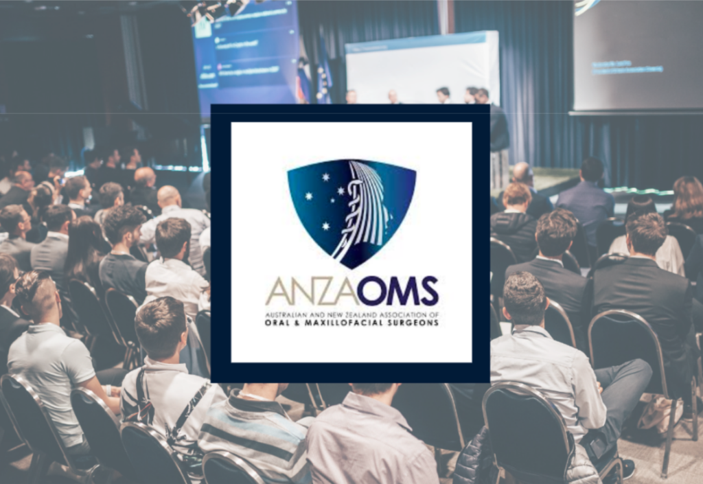 Audience seated in a conference room, watching a presentation. A large logo in the forefront reads "ANZAOMS," with the full name "Australian and New Zealand Association of Oral & Maxillofacial Surgeons." Discussions on commercial loans highlight financial options for practice expansion.